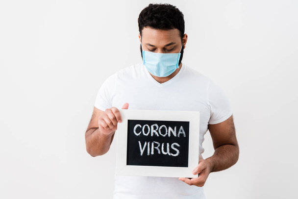 афроамериканський чоловік у медичній масці дивиться на крейдяну дошку з коронавірусною плямою біля білої стіни
  - Фото, зображення
