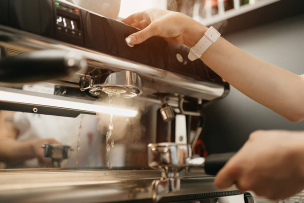Une femme barista purge une tête de groupe à fond avec de l'eau chaude dans la machine à expresso dans un café. Un barista travaille dans un café
. - Photo, image