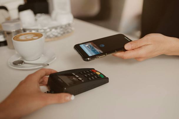 Uma mulher que paga o seu café com um smartphone por tecnologia NFC sem contato em um café. Uma empregada de bar tem um terminal para pagar a um cliente num café.
. - Foto, Imagem