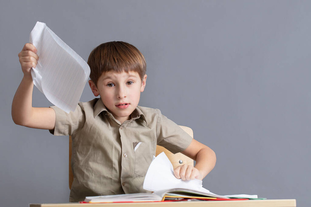 Het kind is boos op huiswerk. Een basisscholier scheurt papier.. - Foto, afbeelding