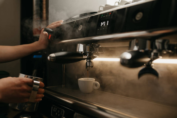 Ein genaues Foto einer professionellen Kaffeemaschine. Ein Barista gießt einen Kaffee in eine weiße Tasse. Dampf um Dampf. - Foto, Bild