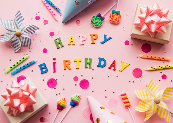 Text Happy Birthday von Holzbuchstaben mit Geburtstagskerzen, Kerzen und Konfetti auf rosa Hintergrund - Foto, Bild