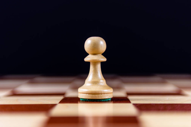white wooden pawn on a chessboard on a black background - Foto, Imagem