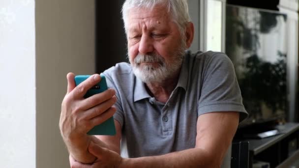 Happy senior elderly man holding smart phone watching mobile video calling online looking at screen - Footage, Video