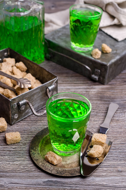 Grüne Flüssigkeit in einem Glas mit Zuckerwürfeln auf dunklem Holzgrund. Selektiver Fokus. - Foto, Bild