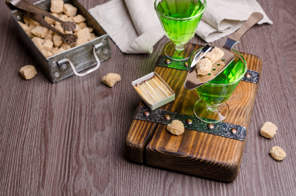 Liquido verde in un bicchiere con cubetti di zucchero su uno sfondo di legno scuro. Focus selettivo
. - Foto, immagini
