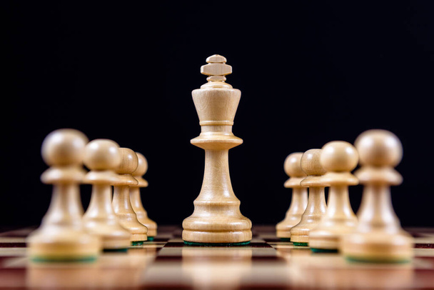 white chess king among white pawns on a chessboard on a black background - Zdjęcie, obraz