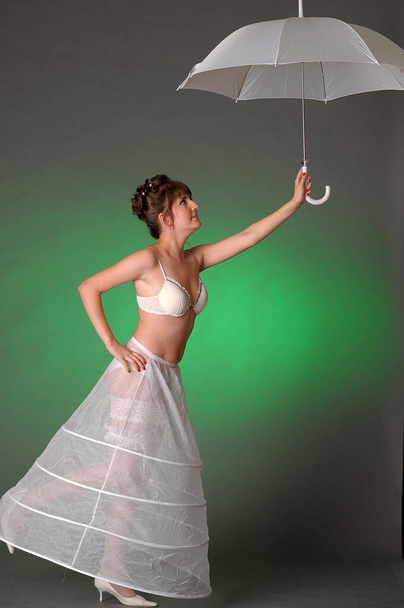 girl in a petticoat with an umbrella on a green background - Фото, зображення