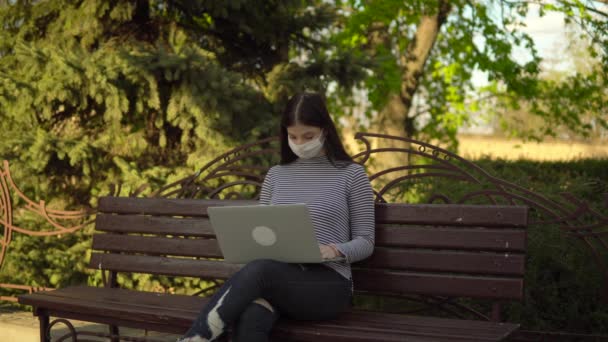 Mujer en máscara de protección médica freelancer trabajando con portátil al aire libre en el parque
 - Metraje, vídeo