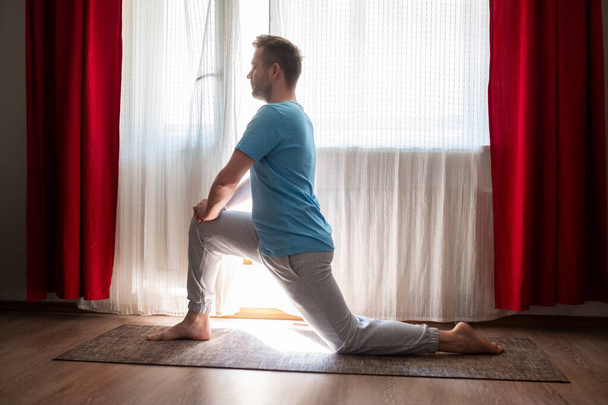 caucasiano homem em Anjaneyasana uma perna lunge pose praticando online em casa
. - Foto, Imagem