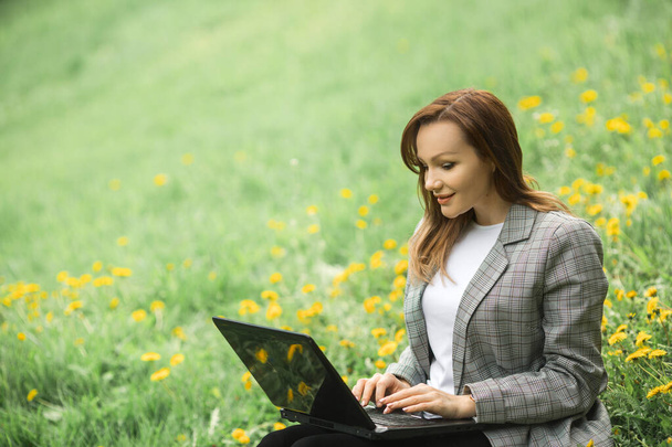 beautiful young woman in a gray jacket with a laptop in the park - Фото, изображение