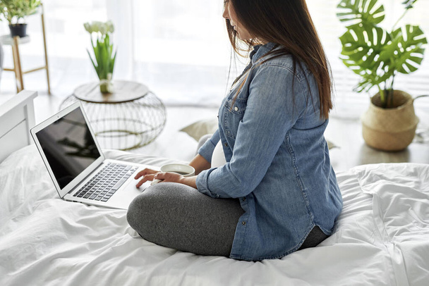 Zwangere vrouw met behulp van een computer tijdens het zitten op bed - Foto, afbeelding