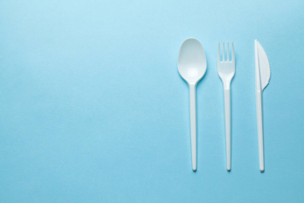 Plastic cutlery, forks, spoons and knives. Pollution of the environment with plastic and microplastics. Blue background. Copy space for text. - Fotoğraf, Görsel