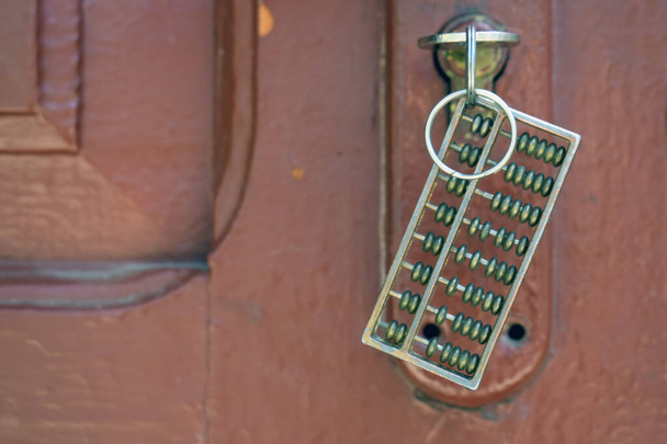 Kis fém abakusz kulcsos kulcstartó formájában. Dekoratív abakusz egy zárban a háttérben egy régi fa ajtó sötét bordó színű. - Fotó, kép