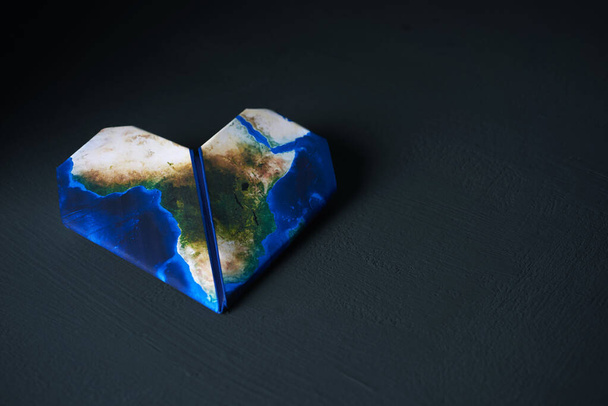 Origamiherz, gemustert mit einer von der NASA eingerichteten Afrika-Karte, auf dunklem, strukturiertem Hintergrund mit einer Leerstelle rechts - Foto, Bild