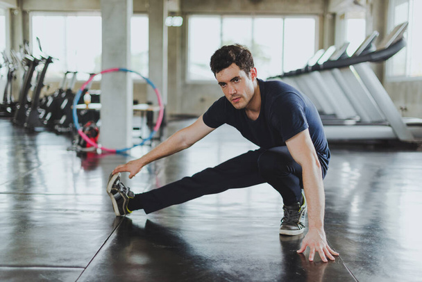 Hombres atléticos estirándose antes de hacer ejercicio sobre colchonetas de yoga en el gimnasio. Estirando los músculos de sus piernas
. - Foto, Imagen