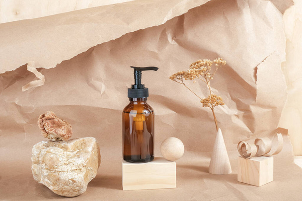 Brown glass bottle with pump of cosmetic products on stone, wooden geometric shapes and dried flowers on beige paper background. Natural Organic Spa Cosmetic Beauty concept Front view Mockup. - Фото, зображення