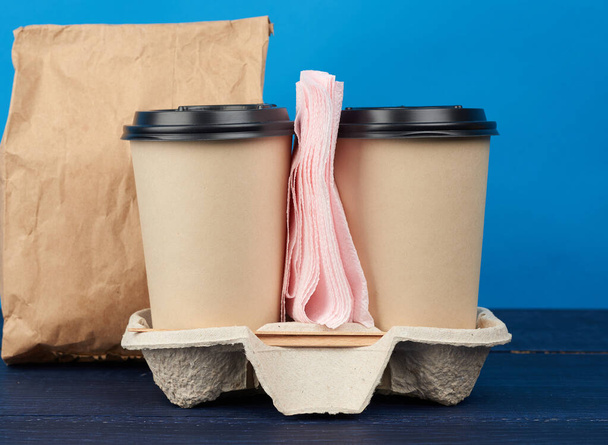 brown paper disposable cups with a plastic lid stand in the tray on a blue wooden table, takeaway containers - Photo, Image