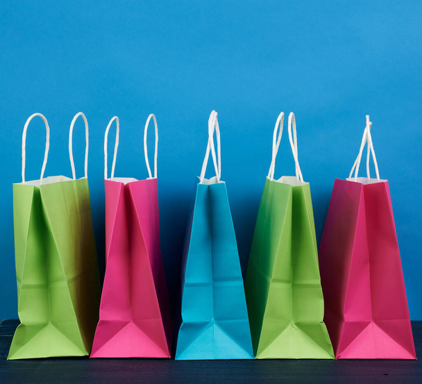 разноцветные бумажные пакеты с ручкой для покупок и подарками на синем фоне
 - Фото, изображение