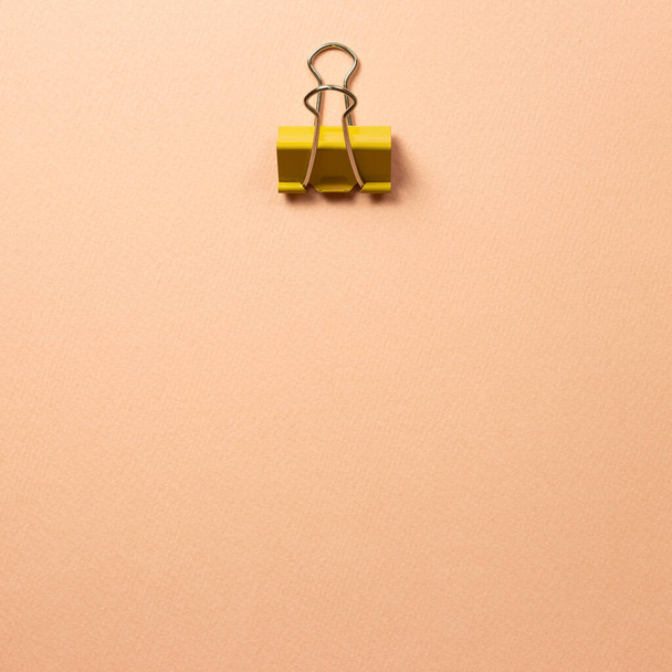 ピンクベージュの背景に黄色の金属バインダークリップ - 写真・画像