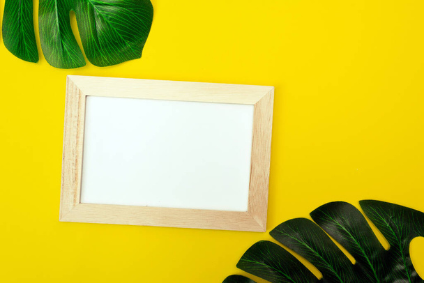 Top view of a white square frame mockup with palm leaf decoration. Summer composition on yellow background. - Zdjęcie, obraz