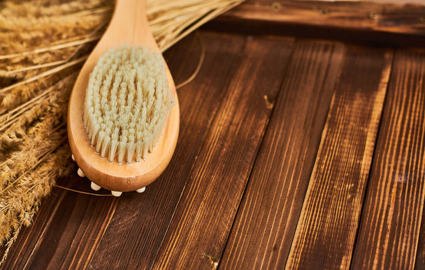 Wooden brush massage counter, washcloth for shower with double body nozzles with bunch of dried straw on dark background with place for inscription.  - Photo, Image
