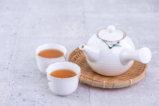 Hot tea in white teapot and cups on a sieve over bright gray cement background, closeup, copy space design concept. - 写真・画像