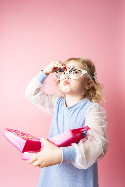 Little girl child plays with a set of children's cosmetics. Studio portrait on a pink background. - Foto, Imagen