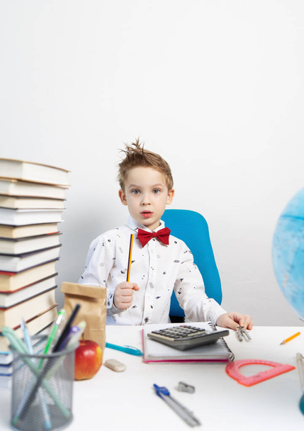 Child education: a little boy in glasses and a red bow tie sits at a desk with a pencil in his hand. Portrait. - Fotografie, Obrázek