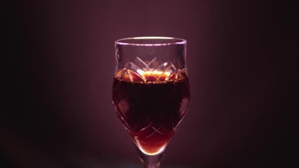 Glass of red wine on a black background with a color cast - Кадры, видео