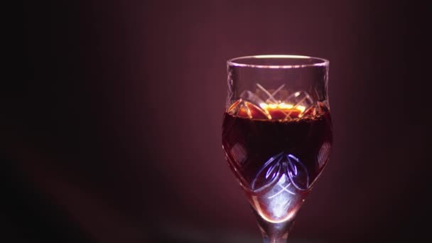 Glass of red wine on a black background with a color cast - Кадры, видео
