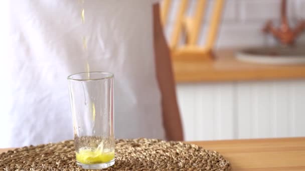 Close-up, woman pours yellow fizzy drink into glass while standing in kitchen - Imágenes, Vídeo