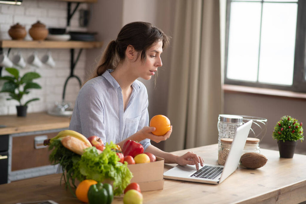 Girl in grey homewear sitting at the table and holding an orange - Foto, Bild