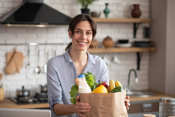 Chica en ropa de casa gris sosteniendo un paquete con comestibles y sentirse positivo
 - Foto, imagen