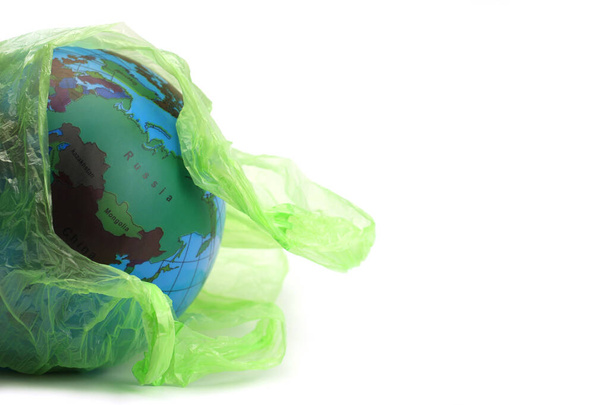 Globe in a plastic garbage bag is isolated on white. Concept of an environmental disaster on the planet - Фото, изображение