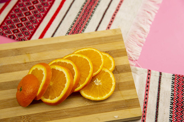 新鮮なオレンジフルーツ全体と木製のテーブルの上にスライス,まな板とキッチンナイフ.柑橘類のスライスでいっぱいのプレート-自然と健康食品。フルーツカクテルのグラス. - 写真・画像