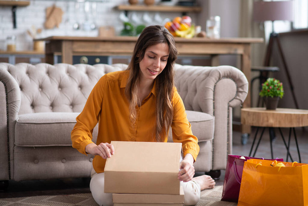 Long-haired girl in a mustard color blouse unpacking a carton - 写真・画像