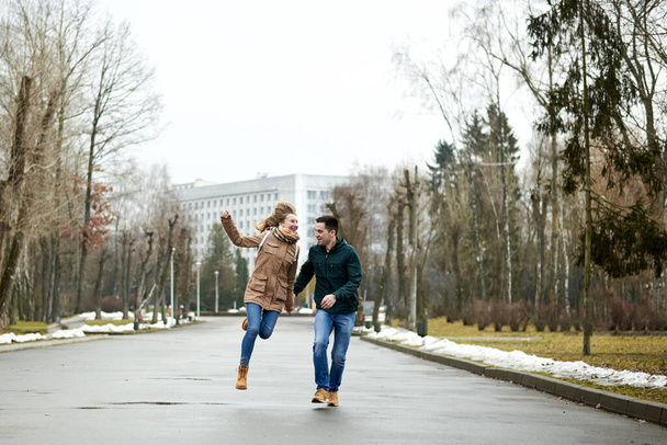 Two young people, wearing casual clothes and jeans, running and jumping, holding hands, laughing, smiling, in spring park. Romantic Valentines day celebration - Foto, Imagem