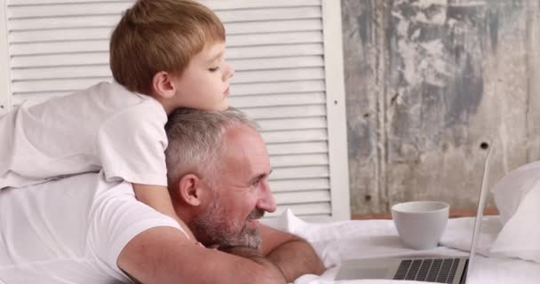 Отец и сын смотрят мультики на ноутбуке, лежащем на кровати
. - Кадры, видео