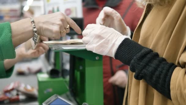 De vrouw in de supermarkt haalt wisselgeld op na het winkelen in rubberen handschoenen. Veiligheidsmaatregelen tegen coronavirusinfectie. - Video