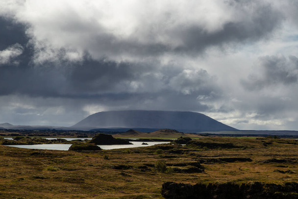 tájkép Izlandon. Az ég tele van felhőkkel, és van egy látható vízpont a vulkáni kövek közepén, tele mohával. - Fotó, kép