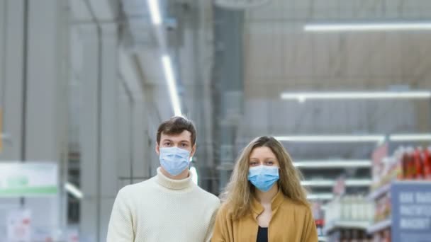 fiatal házaspár orvosi maszk és kesztyű áll a szupermarketben élelmiszerbevásárlókocsi, kamera mozgás, timelapse, elleni védelem coronovírus - Felvétel, videó