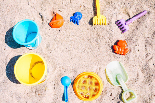 Selection of beach toys on white sandy beach. Top view of colourful hildren's toys to play in sand on family summer vacation. Background with empty space for text. Selective focus - Photo, image