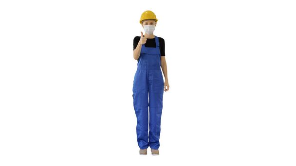 Female construction worker putting on medical mask on white background. - 写真・画像