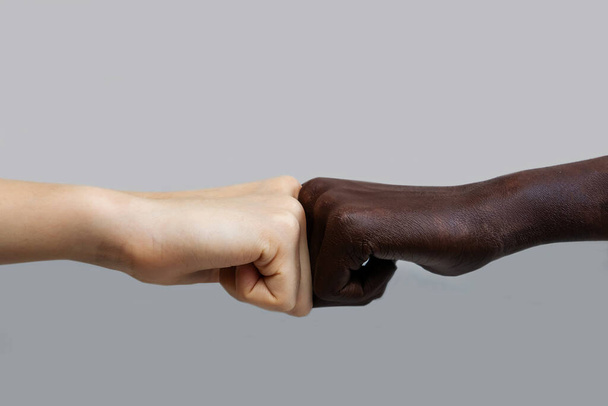 The black African-American hand and the white European hand give a blow to the partnership and cooperation agreement against a grey isolated background.The concept of combating racism. - 写真・画像