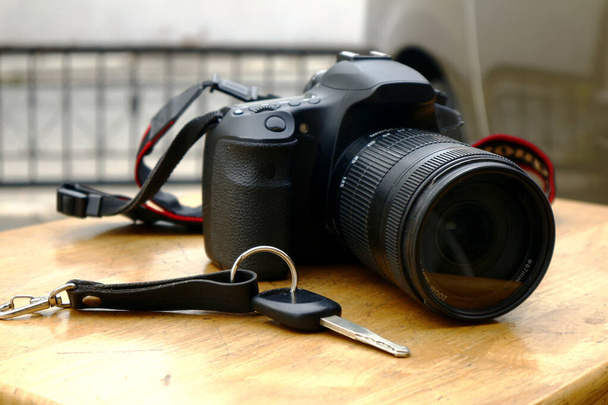 Foto einer digitalen Spiegelreflex- oder DSLR-Kamera und eines Autoschlüssels auf einem Holztisch - Foto, Bild