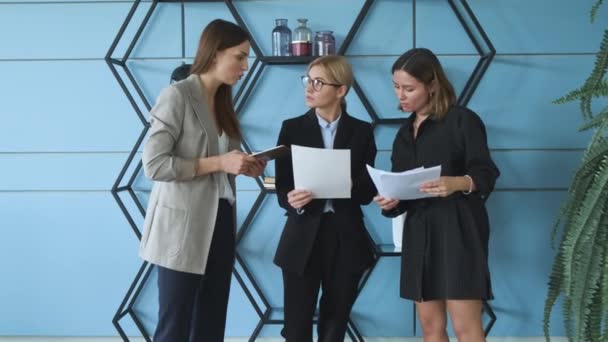 Πλήρης συγκέντρωση στο χώρο εργασίας. Ομάδα νέων επιχειρηματιών επικοινωνούν ενώ στέκονται στο γραφείο συνεδριάσεων του γραφείου μαζί. Τρεις γυναίκες συνάδελφοι διαφωνούν για την άποψη. - Πλάνα, βίντεο