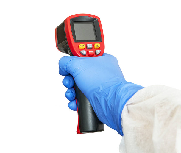 Θερμόμετρο μη επαφής ψηφιακό υπέρυθρο με σκόπευτρο λέιζερ σε ανθρώπινο χέρι φορώντας μπλε προστατευτικά ιατρικά γάντια. Αντικείμενο απομονωμένο σε λευκό φόντο. κενή οθόνη για σχεδιασμό - Φωτογραφία, εικόνα
