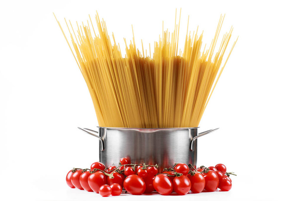 Pasta spaghetti in een metalen pan in een groot collum op een witte achtergrond met tomaten. - Foto, afbeelding