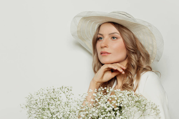 Meditatiivinen nainen yllään kesäkauden hattu tilalla kukkia valkoisella taustalla
 - Valokuva, kuva